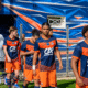 Soccer players in blue and orange uniforms walking out onto the field from a tunnel, with a colorful backdrop behind them.