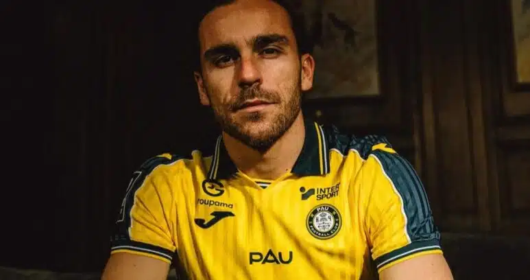 julien-anziani-est-au-sortir-dune-experience-en-turquie-reussie-sportivement-julien-rej-recadree | AllezPaillade.com Man with short dark hair and stubble wearing a yellow PAU football jersey, seated in a dimly lit room.