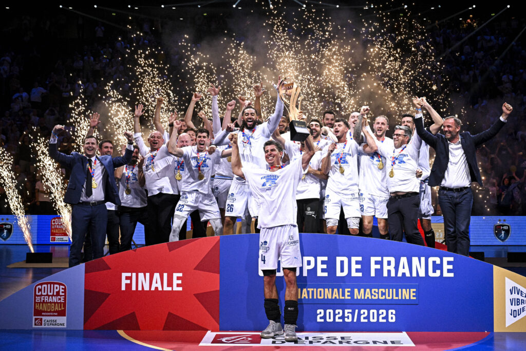 Montpellier Handball v HBC Nantes - Finale Coupe de France Nationale Masculine 20252026 | AllezPaillade.com Handball team on a podium celebrating victory with medals as fireworks explode around them. Crowded arena in the background.