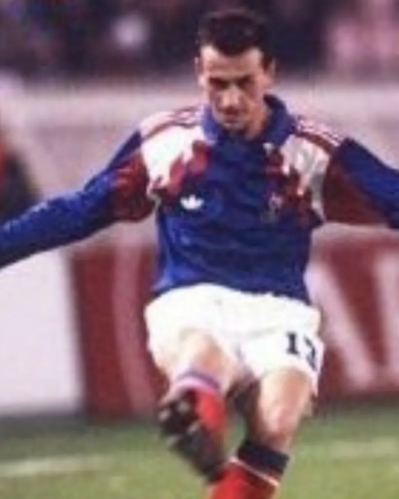 Soccer player in a blue jersey and white shorts kicking a ball during a match, number 11 visible on shorts.