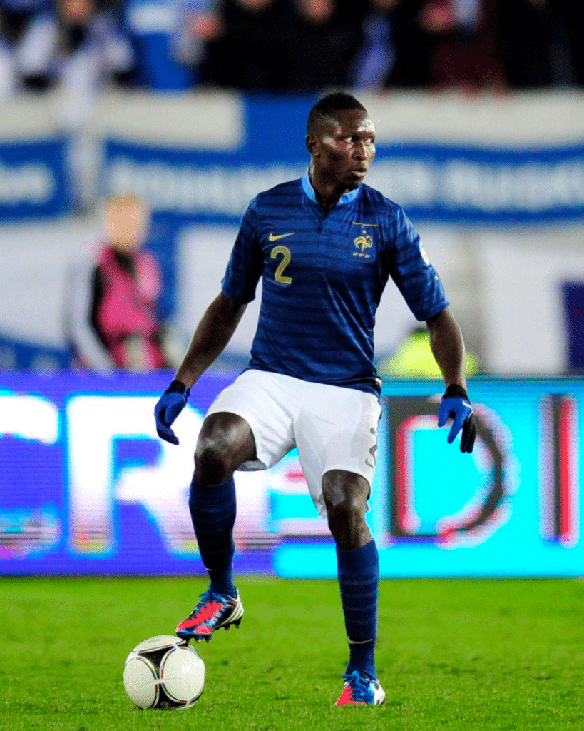 Soccer player in a blue jersey with the number 2, controlling a white ball on a green pitch during a match.
