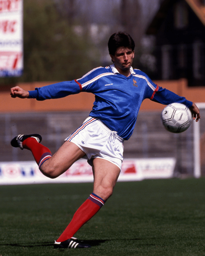 Soccer player in blue jersey and white shorts kicking a ball on a field under bright light.