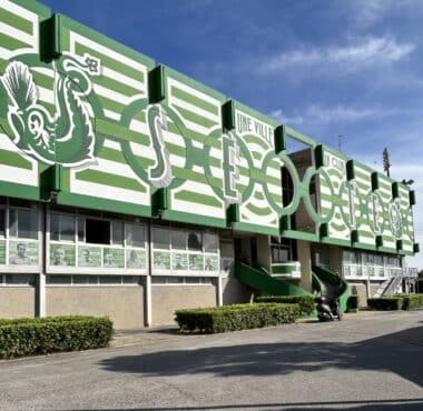 Green and white stadium fa&ccedil;ade with large stylized letters and arches along the front.