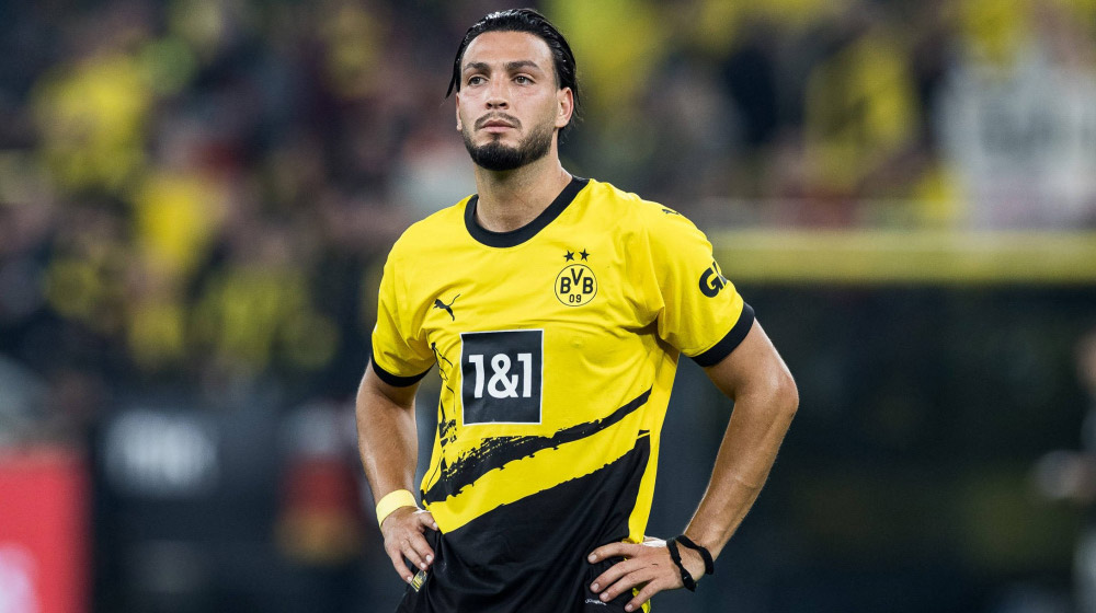 Soccer player in Borussia Dortmund's yellow and black kit standing with hands on hips on the pitch.