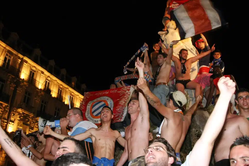 Fete sur la Place de la Comedie | AllezPaillade.com Nighttime street celebration with a crowded group of shirtless men on a decorated float, waving flags and cheering.