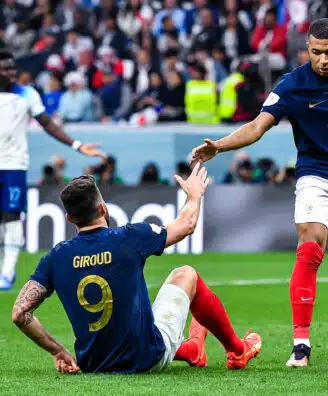 French national-team players celebrate on the field, reaching toward each other for a high-five amid a cheering crowd.