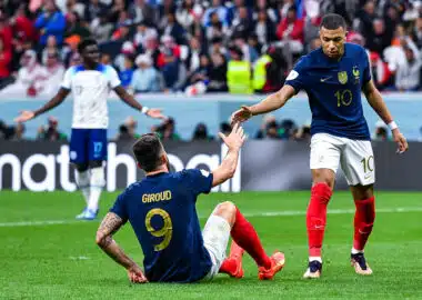 French national-team players celebrate on the field, reaching toward each other for a high-five amid a cheering crowd.