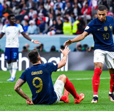 French national-team players celebrate on the field, reaching toward each other for a high-five amid a cheering crowd.