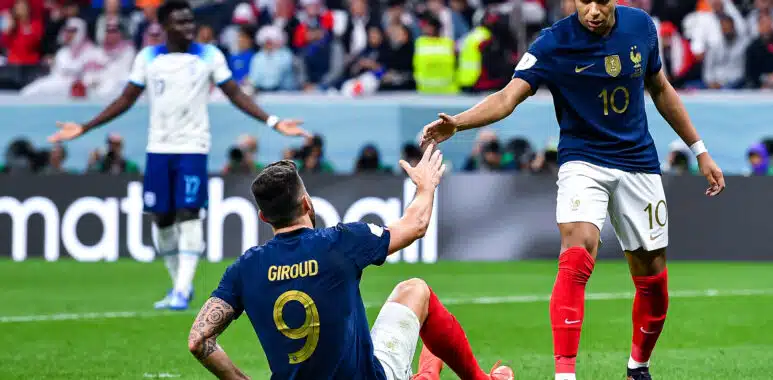 Mbappé Giroud England v France - FIFA World Cup 2022 Quarterfinal | AllezPaillade.com French national-team players celebrate on the field, reaching toward each other for a high-five amid a cheering crowd.