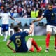 French national-team players celebrate on the field, reaching toward each other for a high-five amid a cheering crowd.