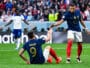 French national-team players celebrate on the field, reaching toward each other for a high-five amid a cheering crowd.