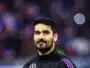 Portrait of a man with dark hair and a beard in a black jacket with purple stripes, standing in a sports arena.