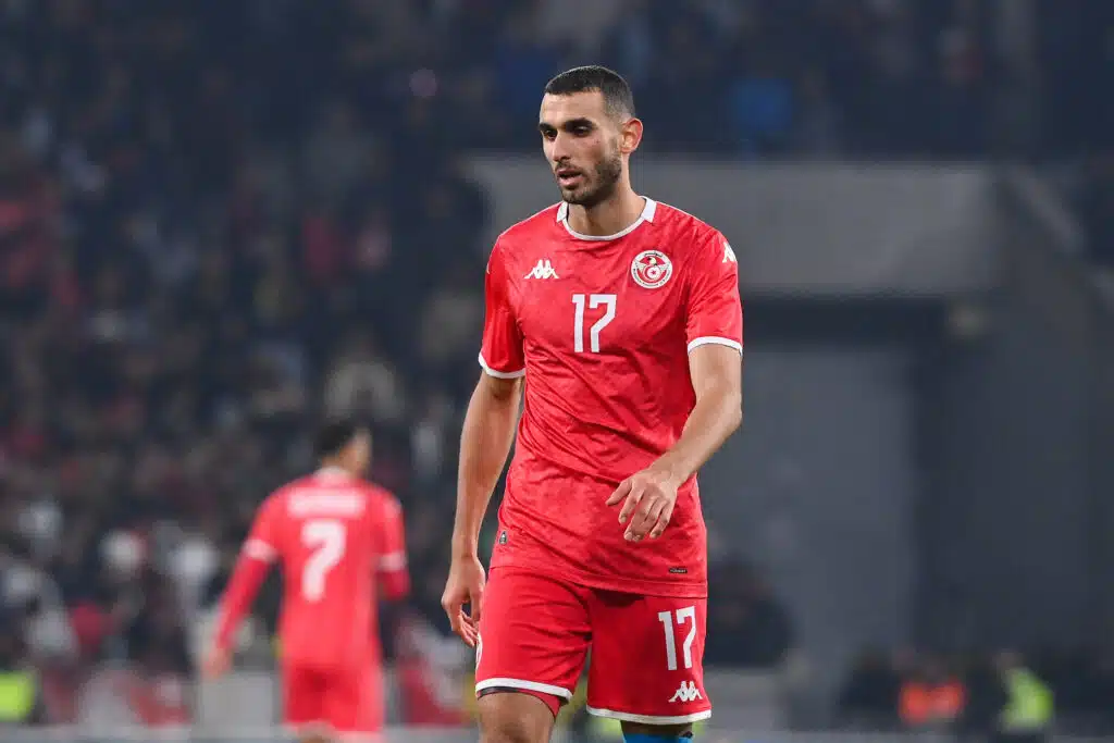 Tunisian national team footballer in a red jersey with number 17 on the field during a match, crowd in the background