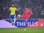 Two soccer players&mdash;Brazil in yellow, Tunisia in red&mdash;jump for the ball during a match, crowd in the stands behind them.