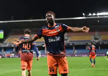 Montpellier Herault SC v Stade Lavallois Mayenne FC - Ligue 2 BKT 20252026 | AllezPaillade.com Soccer player in orange and navy kit celebrates with arms outstretched on a stadium field at night.