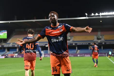 Soccer player in orange and navy kit celebrates with arms outstretched on a stadium field at night.