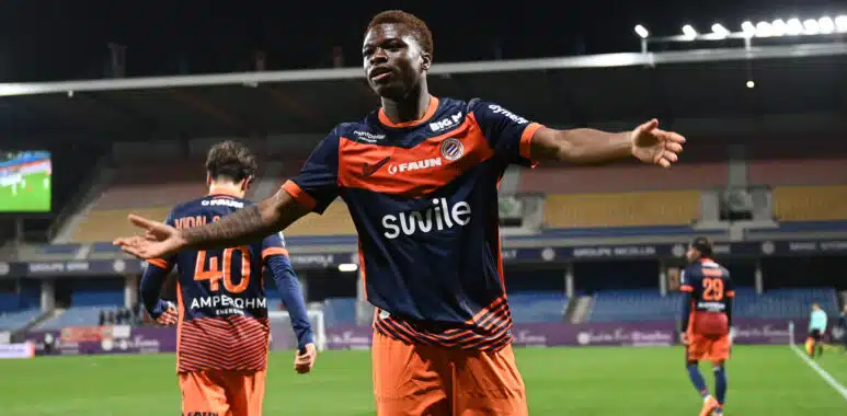 Montpellier Herault SC v Stade Lavallois Mayenne FC - Ligue 2 BKT 20252026 | AllezPaillade.com Soccer player in orange and navy kit celebrates with arms outstretched on a stadium field at night.