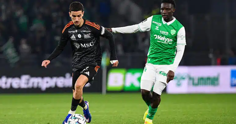 Soccer players contest the ball on a green field; one in black with orange accents, the other in green and white.