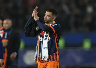 Soccer player in orange and navy kit clapping with a towel over his shoulder on the field after a game?
