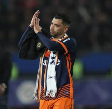 Soccer player in orange and navy kit clapping with a towel over his shoulder on the field after a game?