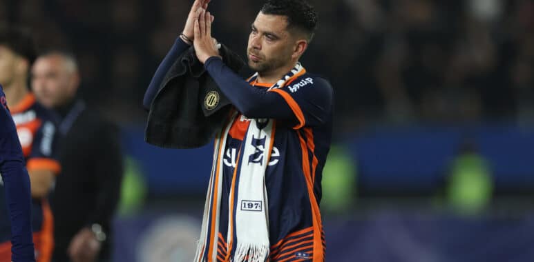 Soccer player in orange and navy kit clapping with a towel over his shoulder on the field after a game?