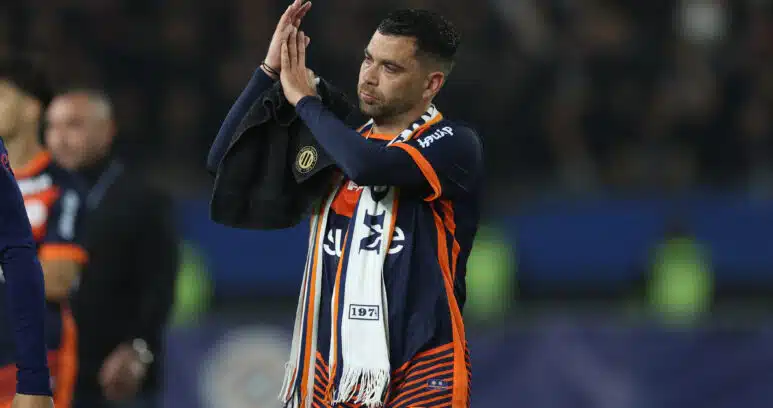Soccer player in orange and navy kit clapping with a towel over his shoulder on the field after a game?