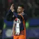 Soccer player in orange and navy kit clapping with a towel over his shoulder on the field after a game?