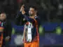 Soccer player in orange and navy kit clapping with a towel over his shoulder on the field after a game?