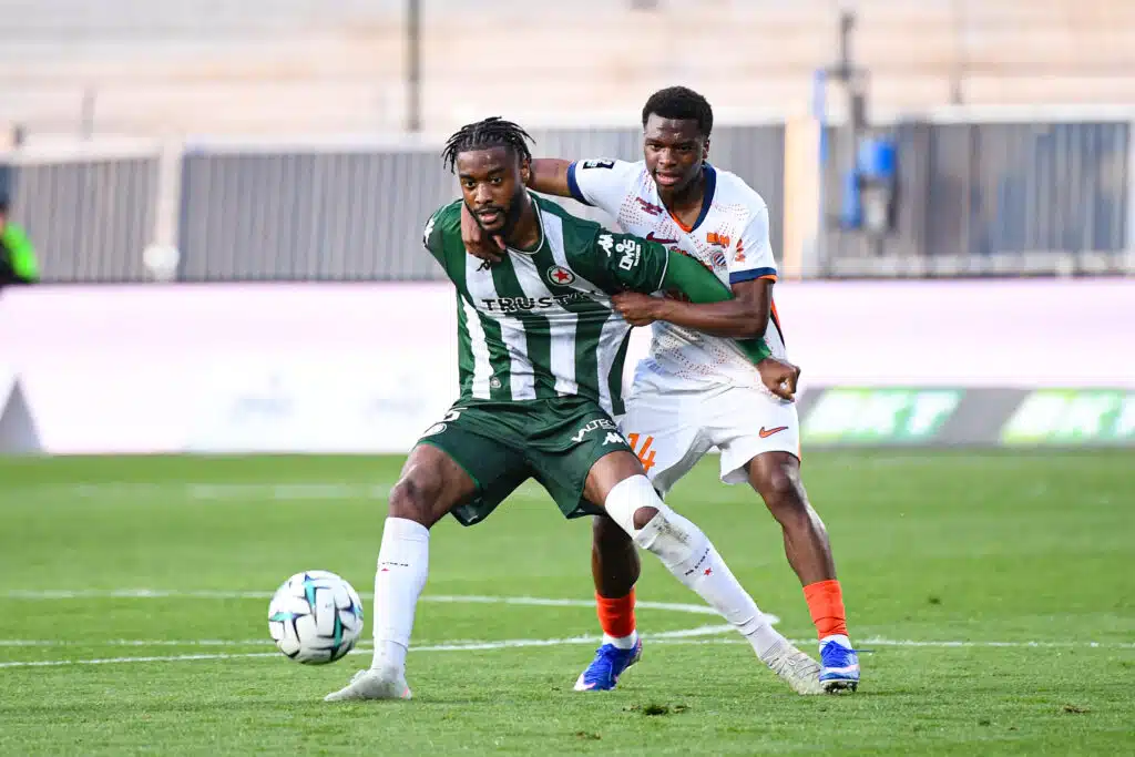 Enzo Molebe Red Star FC v Montpellier Herault SC - Ligue 2 BKT 20252026 | AllezPaillade.com Two soccer players contest the ball during a match, one in green-and-white stripes and the other in white with orange accents.
