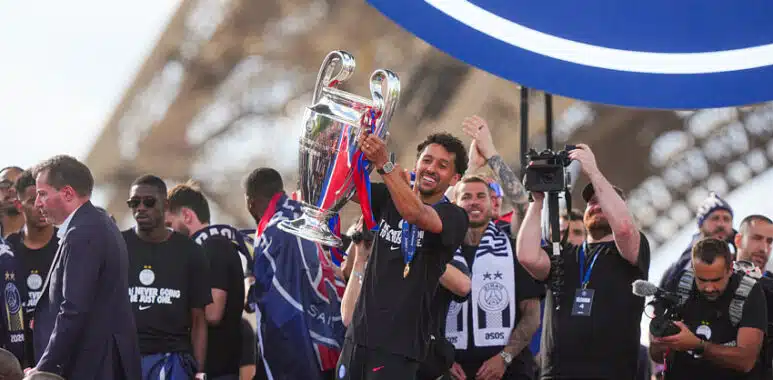 Athlete lifts a silver trophy amid cheering teammates during a victory celebration in a stadium.