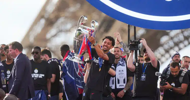 Athlete lifts a silver trophy amid cheering teammates during a victory celebration in a stadium.
