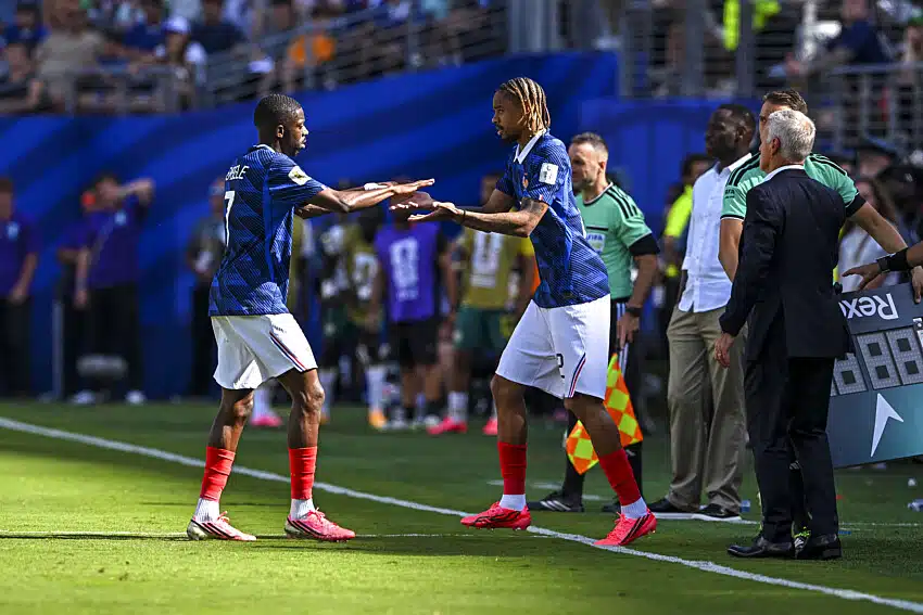 Two soccer players in blue jerseys high-five near the sideline as officials and spectators look on from the field.