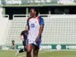 Soccer player in a white jersey with number 20 on a green field, standing with others in the background at a stadium.