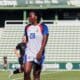 Soccer player in a white jersey with number 20 on a green field, standing with others in the background at a stadium.