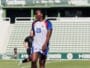 Soccer player in a white jersey with number 20 on a green field, standing with others in the background at a stadium.