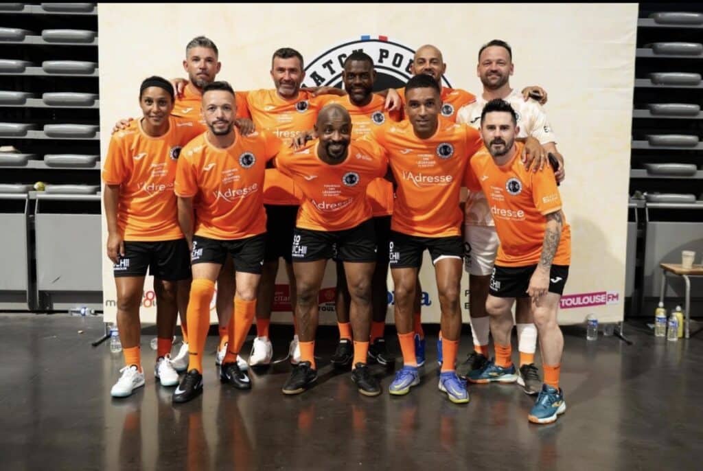 Montpellier Héritage Sport Club | AllezPaillade.com Group of men in bright orange soccer jerseys posing together for a team photo indoors, with a banner behind them.