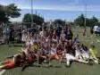 Screenshot | AllezPaillade.com Youth soccer team posing with trophies and medals after a match on a sunny field. Players and coaches celebrate together.