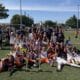 Youth soccer team posing with trophies and medals after a match on a sunny field. Players and coaches celebrate together.