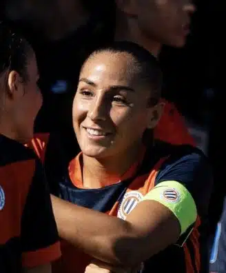 Women&rsquo;s soccer team celebrates, central player smiles while teammates hug.