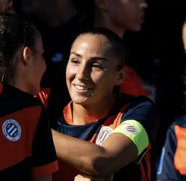 Women&rsquo;s soccer team celebrates, central player smiles while teammates hug.