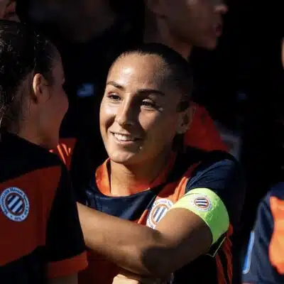 Women&rsquo;s soccer team celebrates, central player smiles while teammates hug.