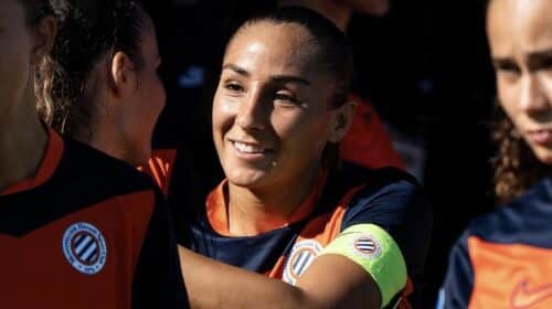 Women&rsquo;s soccer team celebrates, central player smiles while teammates hug.