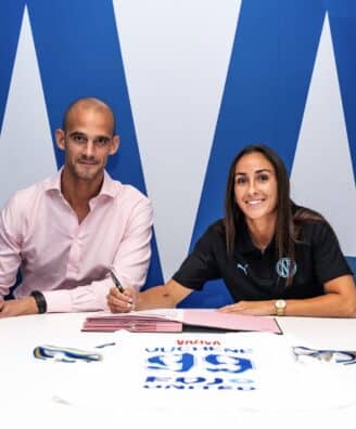 Screenshot | AllezPaillade.com Two professionals signing documents at a white table; man in a pink shirt, woman in black polo, blue backdrop.