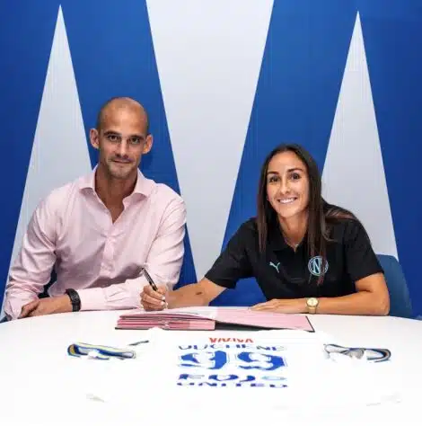 Two professionals signing documents at a white table; man in a pink shirt, woman in black polo, blue backdrop.