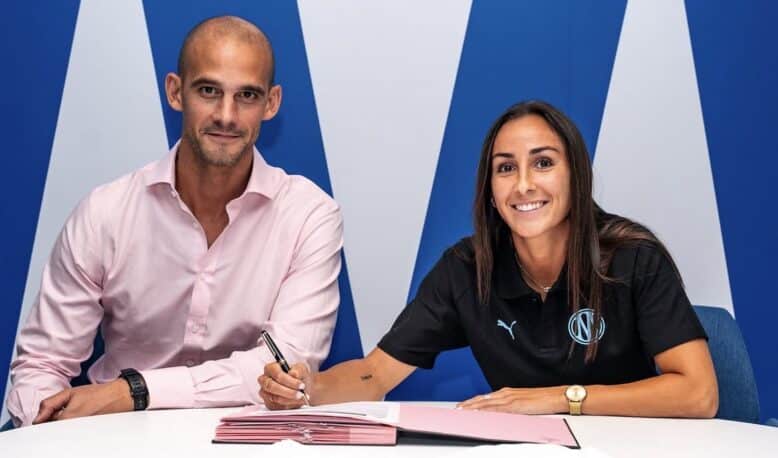 Two professionals signing documents at a white table; man in a pink shirt, woman in black polo, blue backdrop.