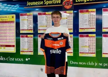 IMG_5118 | AllezPaillade.com Young boy holding an orange and navy soccer jersey in front of a wall of league schedules and charts.