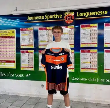 Young boy holding an orange and navy soccer jersey in front of a wall of league schedules and charts.