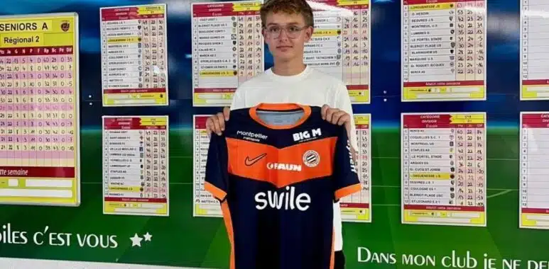 IMG_5118 | AllezPaillade.com Young boy holding an orange and navy soccer jersey in front of a wall of league schedules and charts.