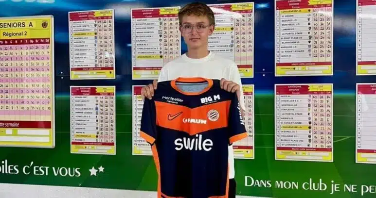IMG_5118 | AllezPaillade.com Young boy holding an orange and navy soccer jersey in front of a wall of league schedules and charts.