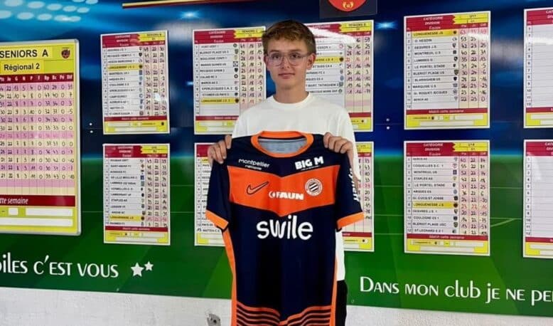IMG_5118 | AllezPaillade.com Young boy holding an orange and navy soccer jersey in front of a wall of league schedules and charts.